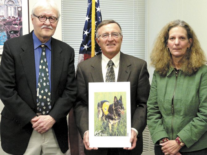 Skaneateles resident Chris Buff, far right, poses with State Sen. John A. DeFrancisco, middle, and artist John Thompson at a Feb. 2 meeting at the senator's Syracuse office during which he gave both Buff and Thompson citations for excellence. DeFrancisco holds a picture of a new $.65 postage stamp depicting Buff's dog, Mittru, a German Shepherd trained as a search and rescue K9.